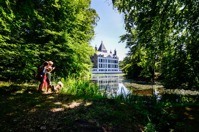 Wandelaars met hond bij de vijver van Kasteel Renswoude, met het kasteel op de achtergrond. De foto combineert cultuurhistorie met wandelen en recreëren in het groene landgoed rondom het kasteel.