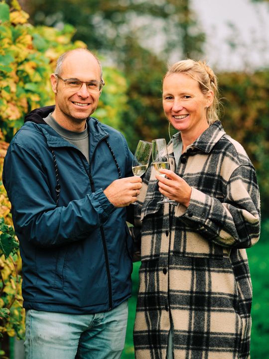 Een man en vrouw toosten met wijn in de wijngaard van Maronesse