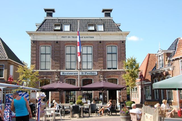 een gebouw met daarvoor allemaal terrassen waar mensen zitten