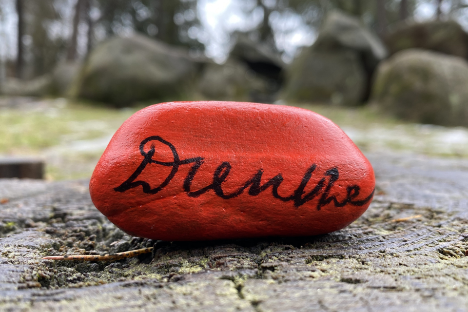 Een rode happy stone met Drenthe met op de achtergrond een hunebed.