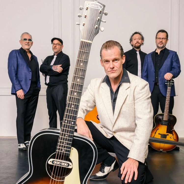 Foto van de band, 5 heren met hun muziekinstrumenten in blauw-zwart-wit gekleed, voor een lichte achtergrond.