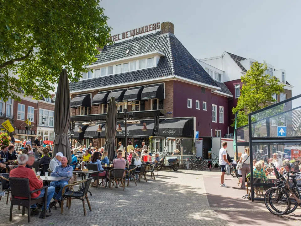 Hotel de Wijnberg in Bolsward op een zonnige dag met op de voorgrond een terras vol met mensen.