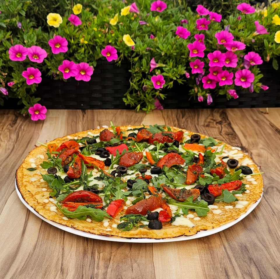 Pannenkoekenrestaurant De Strooppot in De Hoef, Groene Hart. Hartige pannenkoek met rucola, tomaat, paprika en zwarte olijven op een houten tafel met kleurrijke bloemen.
