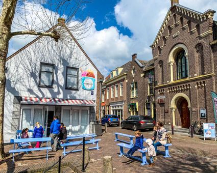 Buitenaanzicht van IJssalon Roberto in pittoresk Oudewater met blauwe bankjes ervoor waarop mensen en kinderen zitten.