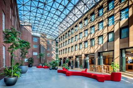 Foto van een met glas overdekte open ruimte (atrium). Zichtbaar zijn de ramen van de hotelkamers in de gevel rechts en rode banken in het midden.