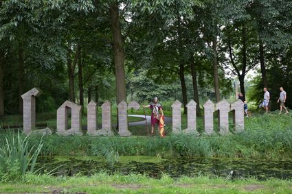 Letters Laurium in het Brediuspark in Woerden met een persoon verkleed als Romeinse soldaat en wandelaars op de achtergrond.