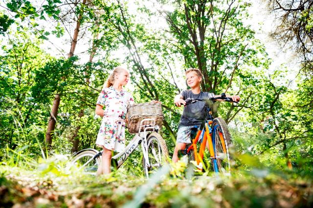 Een jongen en meisje staan met hun fiets in het bos.