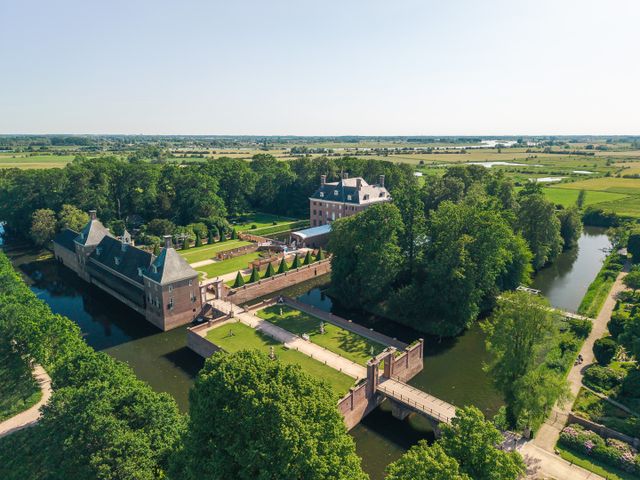 Een indrukwekkend dronebeeld van Kasteel Amerongen, omringd door de slotgracht, historische tuinen en groene bomen. Op de achtergrond strekt het weidse landschap van de uiterwaarden zich uit tot aan de horizon.