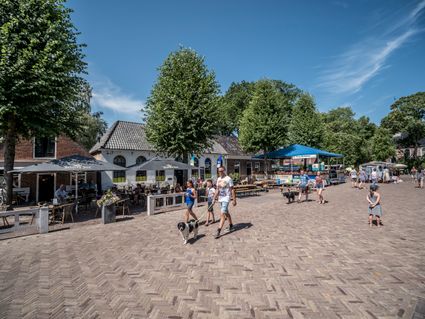 Een winkelstraat in Oudemirdum, aan de overkant is een kleine markt. bij de kraampjes staan mensen te kijken naar de spullen.