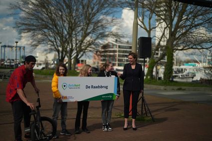 Drie kinderen die een bord vasthouden met de tekst fietshart en raadsbrug, daarnaast houd een mevrouw een microfoon voor een van de kinderen zodat zij wat kan vertellen.