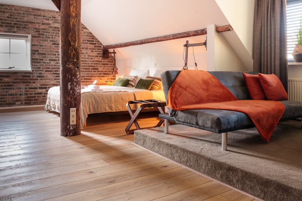 Ein geräumiges Hotelzimmer mit einer authentischen Steinmauer, Holzbalken und Holzboden.