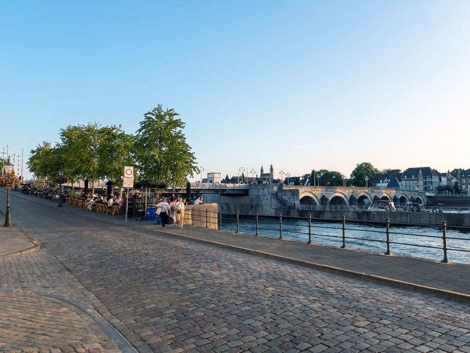Zicht op de Oeverwal in Maastricht met terrasjes langs de Maas en de iconische Sint Servaasbrug op de achtergrond. Op deze historische locatie bevindt zich Het Stookatelier, direct aan het water met uitzicht op de oude binnenstad.