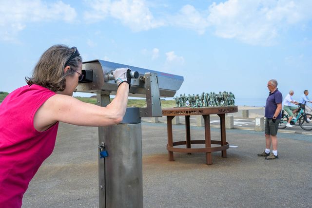 Een vrouw kijkt door een kijker naar de uitlaat van de Rijn, waar ooit het fort de Brittenburg lag.
