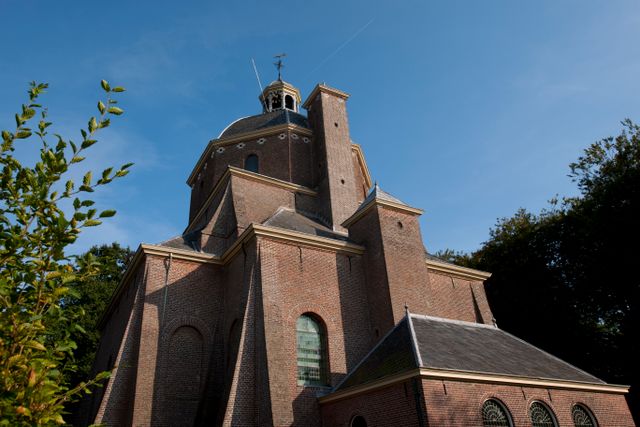 Historische Koepelkerk in Renswoude, gefotografeerd vanaf de zijkant tegen een blauwe lucht. De foto laat de markante bakstenen architectuur en het karakteristieke kerkgebouw in de dorpskern van Renswoude zien.