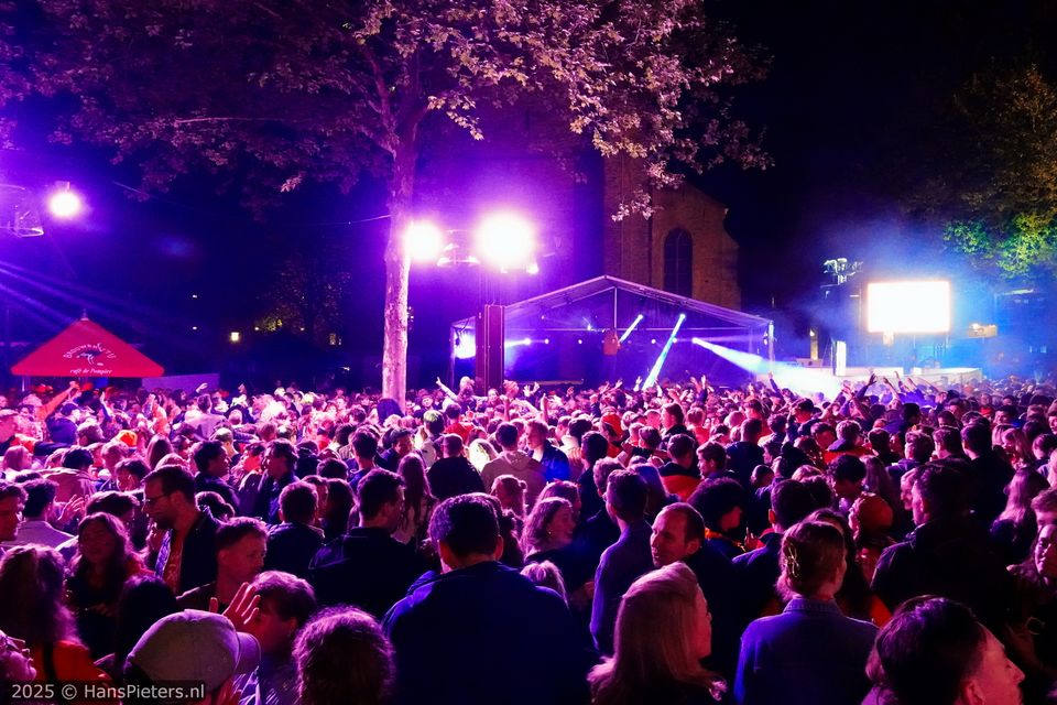 Publieksevenement Koningsnacht in Woerden, Groene Hart, feestende menigte voor een verlicht podium met dj en paarse podiumverlichting op het Kerkplein in de binnenstad.
