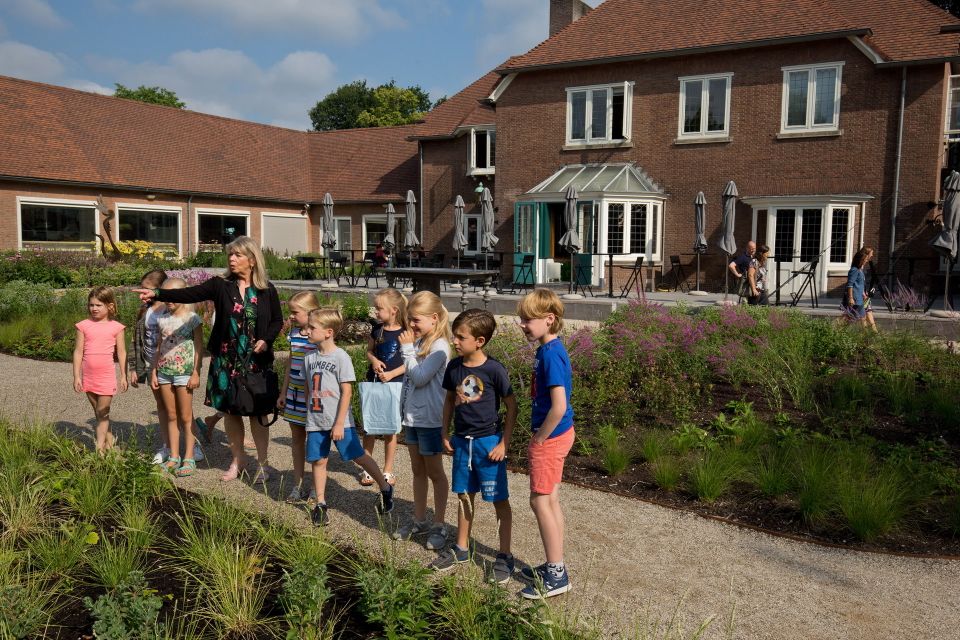 Kinderen op ontdekkingstocht in de museumtuin van Singer Laren samen met een begeleider, die iets interessants buiten het beeld aanwijst.