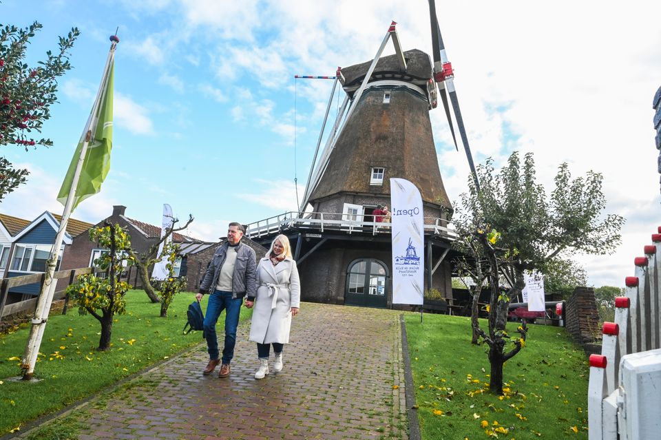 Een stel wandelt bij historische Molen de Valk in Montfoort, met groene grasvelden en fruitbomen eromheen. De molen staat open voor bezoekers en vormt een sfeervolle plek in de Utrechtse Waarden om te wandelen en te genieten van het landschap.