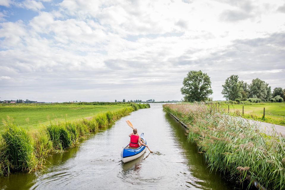 Een kanovaarder vaart door de sloot weg.