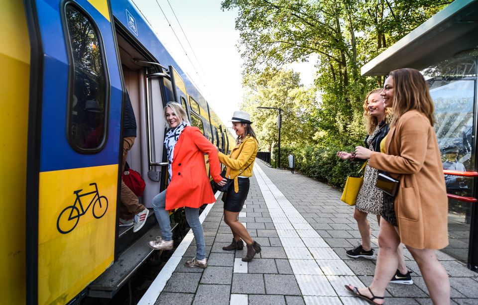Een groep vriendinnen stapt lachend in de trein voor een gezamenlijk dagje uit. De foto straalt plezier uit en laat zien hoe de regio gemakkelijk per openbaar vervoer te ontdekken is.