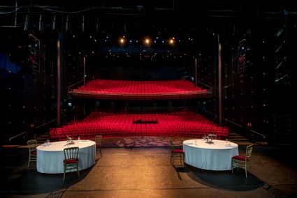 Theaterzaal met twee tafels op het podium en stoelen op het podium en een lege theaterzaal.