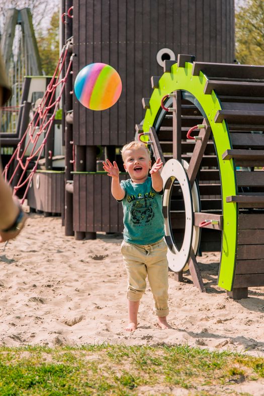 Jongen speelt met een bal bij een speeltoestel.
