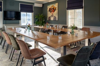 Vergaderlocatie Plein 7 in Woerden, Groene Hart, lichte vergaderzaal voor zakelijke bijeenkomsten met U-opstelling van houten tafels, comfortabele stoelen, televisie en sfeervolle decoratie.