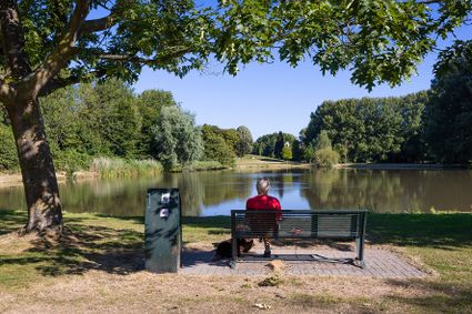 We kijken uit over de grote plas in park Oudegein op een zomerse dag. Voor ons zit een man op een bankje, we kijken op zijn rug.