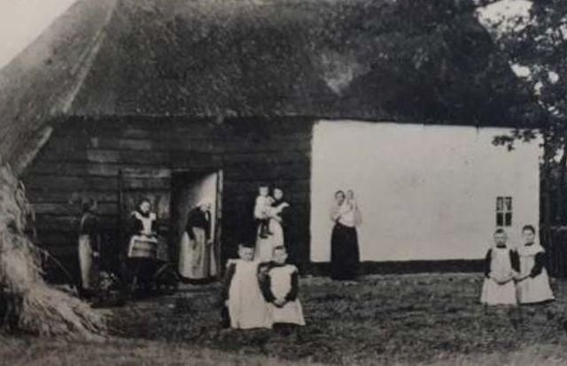 Eine Familie mit vielen Kindern steht vor einem Koloniehaus in Drenthe.