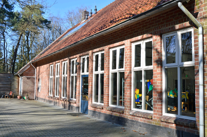 Voorkant van het Natuurvriendenhuis met veel ramen en een blauwe deur.