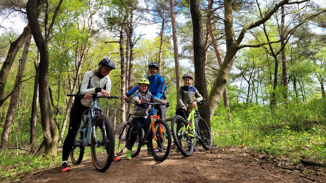 Gezin met kinderen staat met mountainbikes op een bospad op de Utrechtse Heuvelrug. De foto laat samen mountainbiken en actief recreëren in de natuur zien.