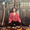 Op de foto is Daphne Posthuma van Praktijk Wad 'n Klank te zien. Ze zit tussen haar klankschalen en andere instrumenten zoals een drum, rainstick en een sansula. Ze is er klaar voor om haar klankschaalconcert te starten.