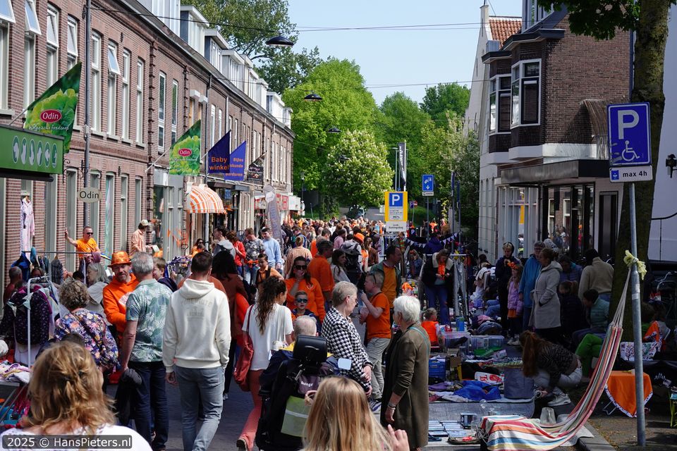 Straatevenement Koningsdag in Woerden, Groene Hart, drukbezochte vrijmarkt met kraampjes, kleedjes en verkopers in oranje kleding in een winkelstraat in de historische binnenstad.