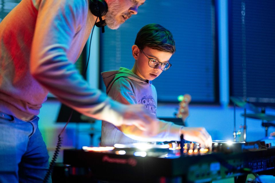Muziekschool Muziekhuis in Oudewater, Groene Hart, DJ-les waarbij een jongen met koptelefoon en DJ-controller leert mixen onder begeleiding van een docent in een muziekstudio.