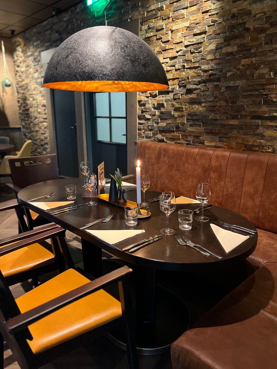 Sfeervol gedekte tafel in het restaurant van Het Wapen van Harmelen, met warme verlichting en een karakteristieke stenen wand.