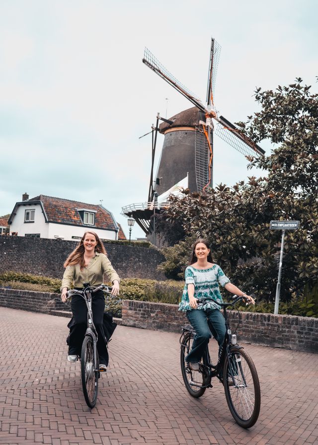 Korenmolen De Windotter, IJsselstein, Groene Hart. Twee fietsers rijden over het Molenplantsoen met de historische korenmolen op de achtergrond, tussen het groen en de oude bebouwing in de binnenstad.
