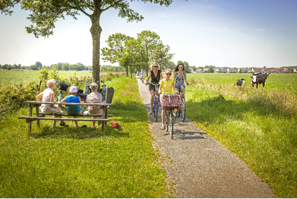 Fietsers en wandelaars genieten van een zomerse dag in het Groene Hart met een rustpunt langs het pad en koeien in de wei.