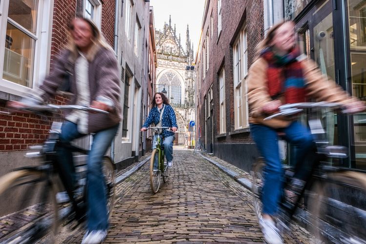 Meiden fietsen door steegje in 's-Hertogenbosch met doorkijkje op Sint-Janskathedraal