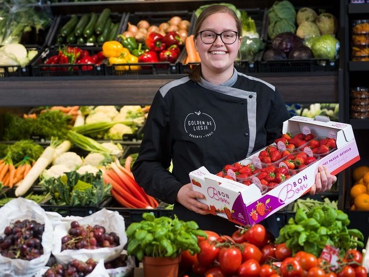 Meisje met kist met aardbeien in haar armen