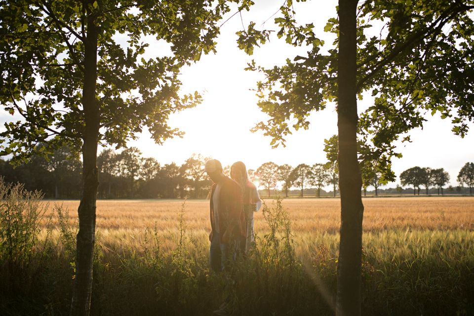 Een stel loopt in de avondzon tussen de bomen door langs een korenveld.