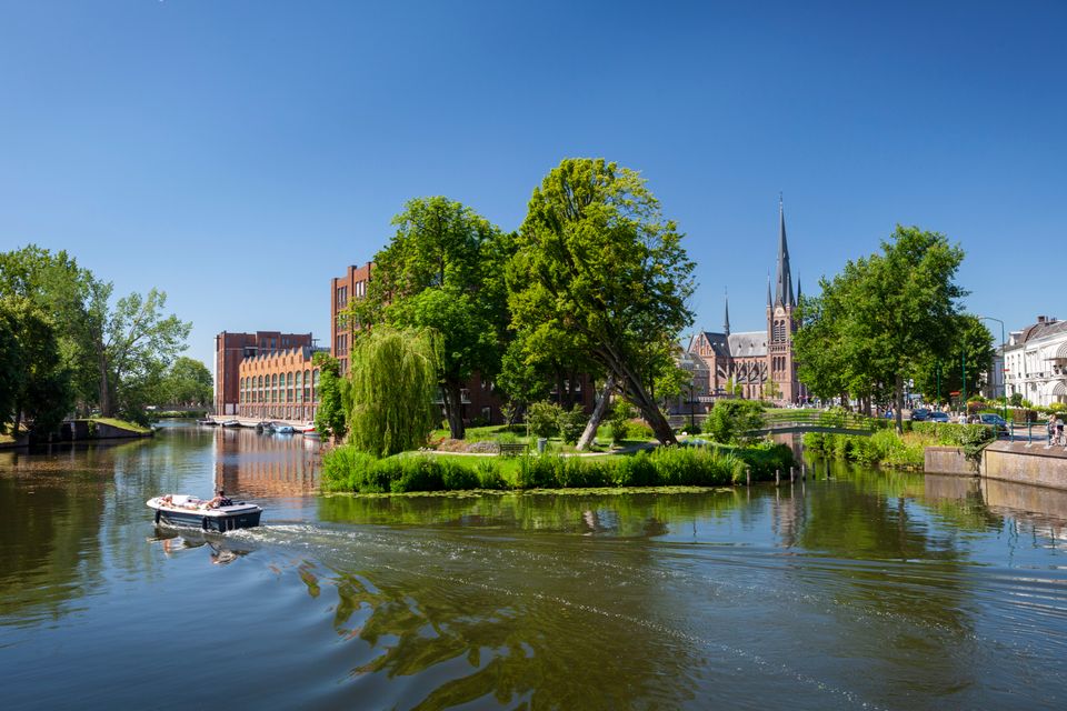 Sloep op de Singel in Woerden, historische vestingstad in het Groene Hart, met uitzicht op Defensie-eiland en de Bonaventurakerk tijdens een zonnige vaartocht door de binnenstad.