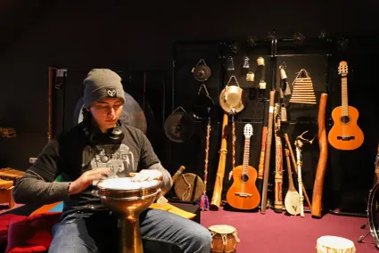Jongen die op een djembe speelt met allerlei muziekinstrumenten achter zich