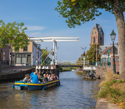 Rondvaartboot De Geelbuik met toeristen op de gracht van Oudewater, met op de achtergrond de ophaalbrug en de Petruskerk in het Groene Hart.