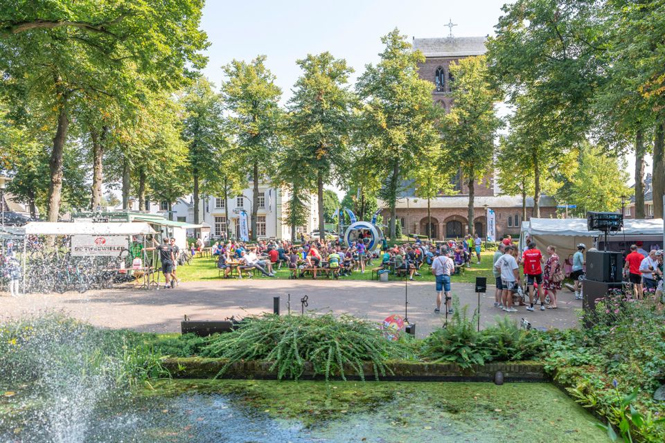 Wielrenners die na afloop van hun deelname een drankje en hapje doen op het grasveld bij de kiosk op De Lind in Oisterwijk. Ook is er muziek.