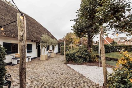 Evenementen- en vergaderlocatie De Willemshoeve in Woerden, Groene Hart, historische hoeve met rieten dak, groene tuin, klinkerterras en sfeerverlichting.