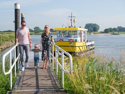 Een vader, kindje en moeder lopen hand in hand over een brug, op de achtergrond staat een geel pondje.
