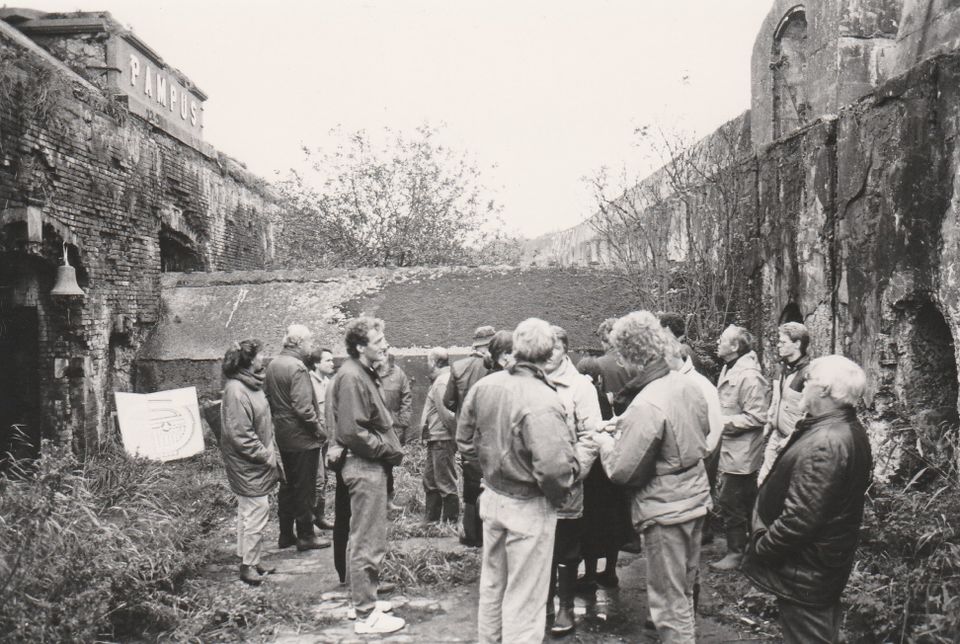 Zwartwit foto van een rondleiding op Pampus in 1991. Het fort is duidelijk vervallen en overgroeid.