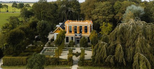 Je ziet een landhuis met parktuin