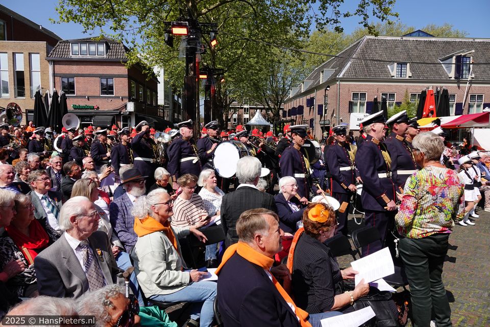 Cultureel evenement Koningsdag in Woerden, Groene Hart, harmonieorkest in uniform met trommels en blaasinstrumenten tijdens een herdenkings- en feestmoment op een plein in de historische binnenstad met publiek in oranje.