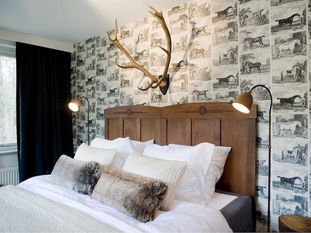 Hotelkamer met groot bed tegen achterwand met zwart-wit behang en een hertengewei boven het bed.