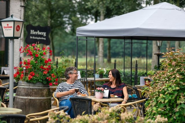 Stel zit lachend op het terras met een kopje koffie en appelgebak.